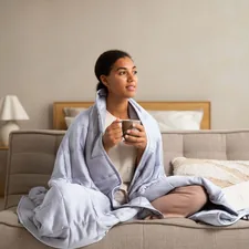 a woman sitting on a couch holding a cup of coffee related to The Ultimate Guide to Choosing the Perfect Bed, Chair, and Pillow for Optimal Comfort