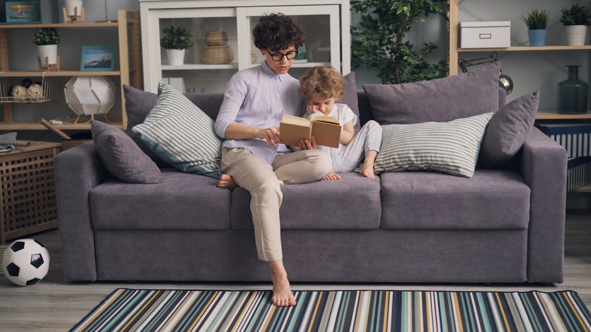 a woman sitting on a couch reading a book to a child related to Cozy Up to Savings: Sofa Bed Sale You Won't Want to Miss