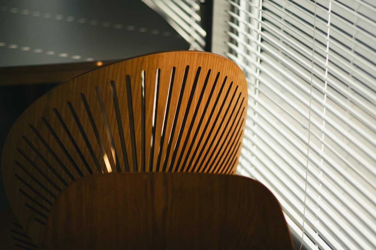 A wooden chair sitting in front of a window related to Wood Blinds: Reliable & Stylish Valance Clips for Perfect Window Coverings