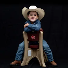 a young boy wearing a cowboy hat sitting on a chair related to Western Baby Bedding Essentials