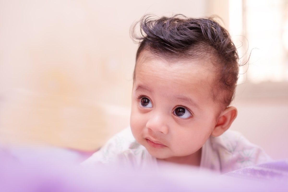 Adorable baby with dark, stylish hair looking upwards. related to Charming Nursery Looks with Elegant Hues