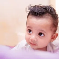 Adorable baby with dark, stylish hair looking upwards. related to Charming Nursery Looks with Elegant Hues