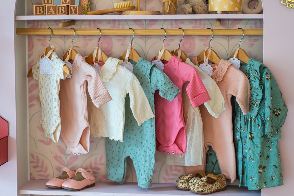 Baby clothes hanging on a rack with shoes below shoes. related to Valances for Nursery