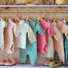 Baby clothes hanging on a rack with shoes below shoes. related to Valances for Nursery