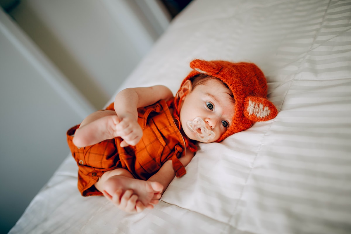 baby in orange knit cap lying on white bed related to Citrus Sweet Dreams:  The Delightful World of Orange Baby Bedding