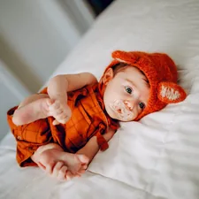 baby in orange knit cap lying on white bed related to Citrus Sweet Dreams:  The Delightful World of Orange Baby Bedding