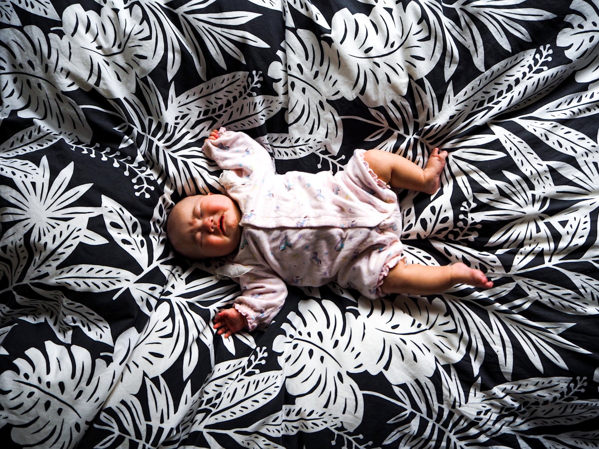 baby in pink onesie lying on black and white zebra print textile related to Creating a Safe Haven: Choosing the Perfect Baby Crib Bedding