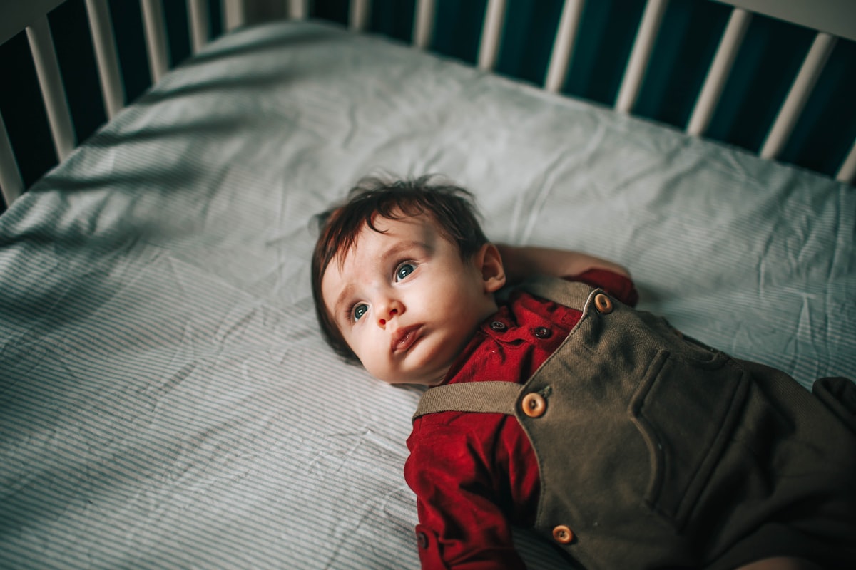 baby in red and gray jacket lying on white bed related to Creating a Dream Nursery: The Ultimate Guide to Boy Crib Bedding