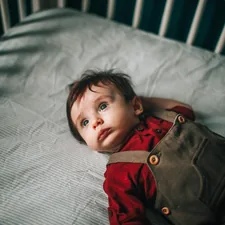 baby in red and gray jacket lying on white bed related to Creating a Dream Nursery: The Ultimate Guide to Boy Crib Bedding