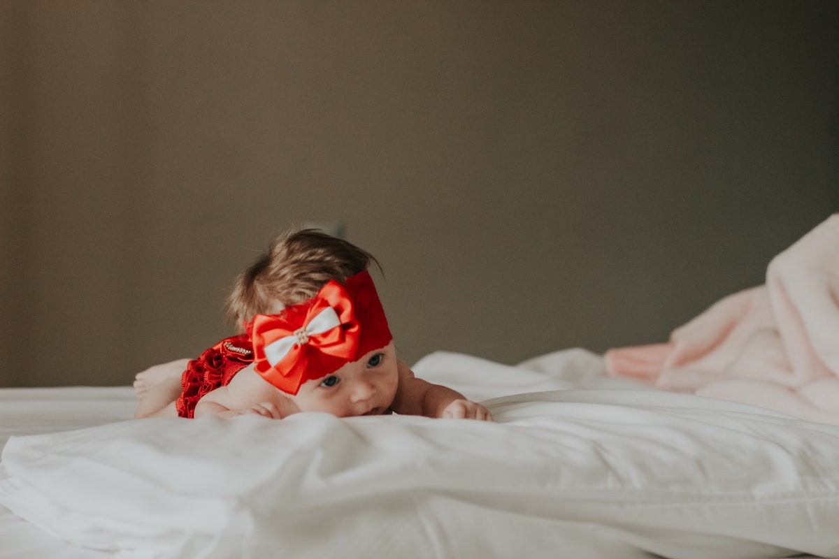baby in red and white polka dot dress lying on bed related to Cutest Baby Girl Bedding Trends to Follow in 2024