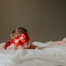 baby in red and white polka dot dress lying on bed related to Cutest Baby Girl Bedding Trends to Follow in 2024