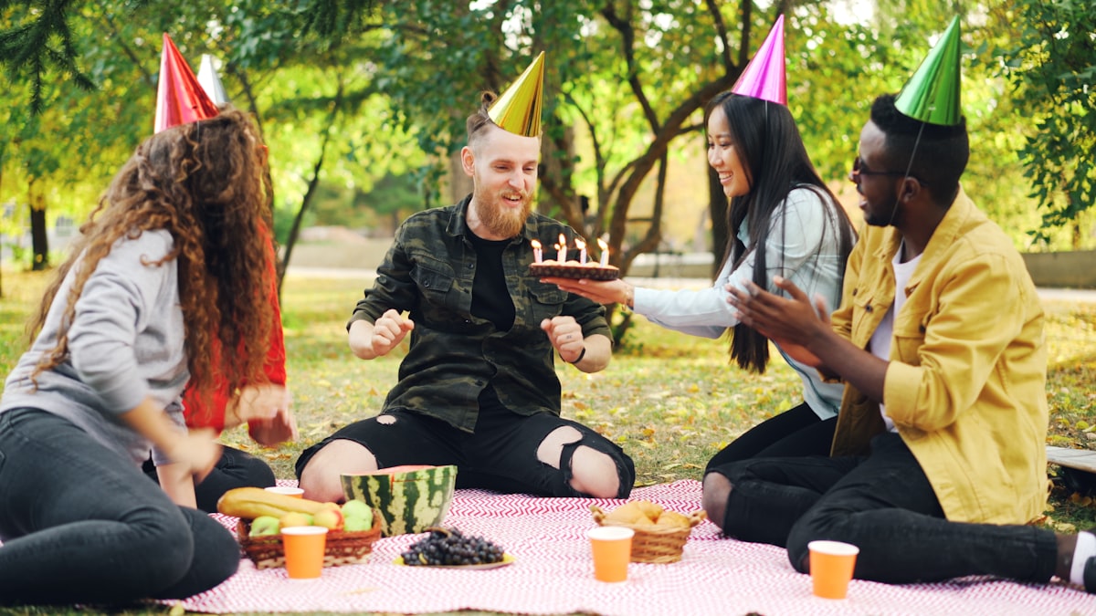 Bearded young man is celebrating birthday with friends in park blowing candles on cake shouting and expressing positive emotions while friends are laughing and clapping hands. related to Transform Your Sleep Space with Fun Bed Sheets