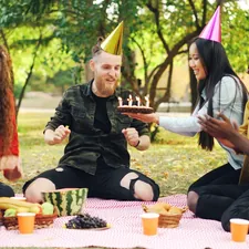 Bearded young man is celebrating birthday with friends in park blowing candles on cake shouting and expressing positive emotions while friends are laughing and clapping hands. related to Transform Your Sleep Space with Fun Bed Sheets