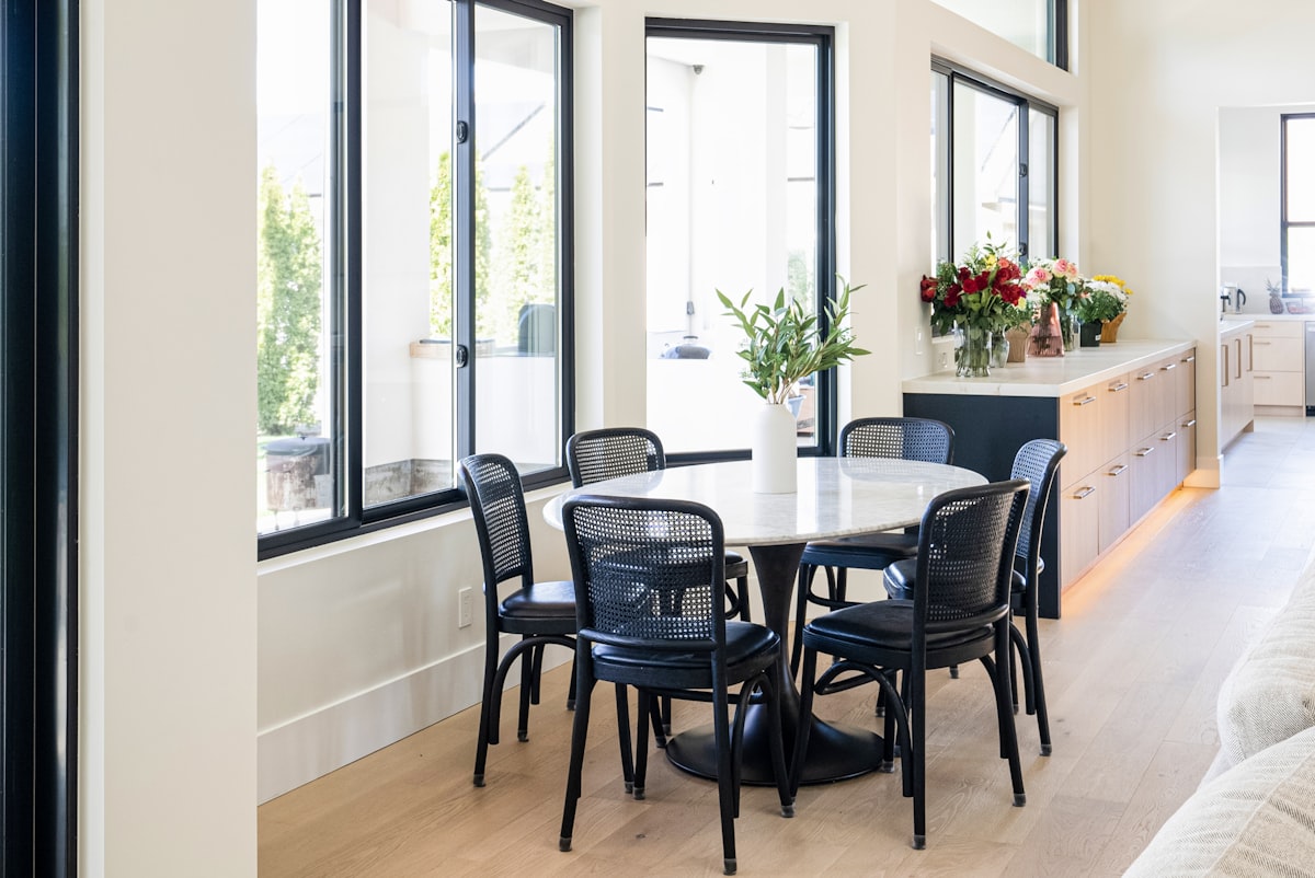 Bright modern dining area with round marble table, black woven chairs, and large floor-to-ceiling windows. Contemporary open-concept home featuring warm wood cabinetry, quartz countertops, and natural light throughout. Elegant residential interior blending minimalist design with organic materials. related to Elevate Your Dining Space: The Ethan Allen Sideboard