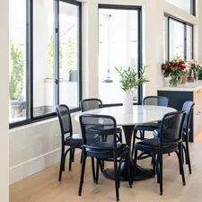 Bright modern dining area with round marble table, black woven chairs, and large floor-to-ceiling windows. Contemporary open-concept home featuring warm wood cabinetry, quartz countertops, and natural light throughout. Elegant residential interior blending minimalist design with organic materials. related to Elevate Your Dining Space: The Ethan Allen Sideboard