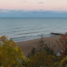 Calm ocean waves lap a sandy beach with autumn trees. related to Exploring the Charm: Bed and Breakfasts in Michigan