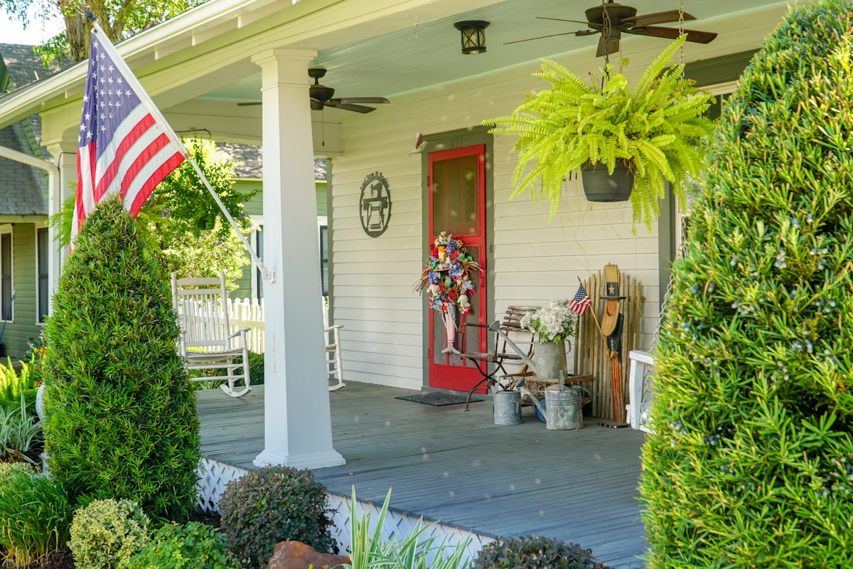 Classic southern American farmhouse front porch decorated for a summer 4th of July celebration. related to Country Chic Window Treatments: Elevating Your Porch with Beautiful Valances
