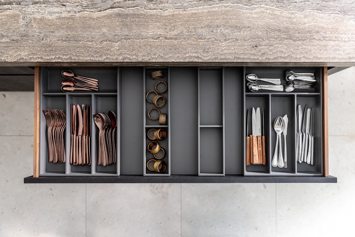 Copper and silver cutlery in an organized wooden kitchen drawer related to Elegant Storage Solutions: The Black Sideboard Table