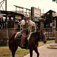 Cowboy on horseback holding a lasso in a western town related to Discover the Urban Cowboy Bed and Breakfast Experience