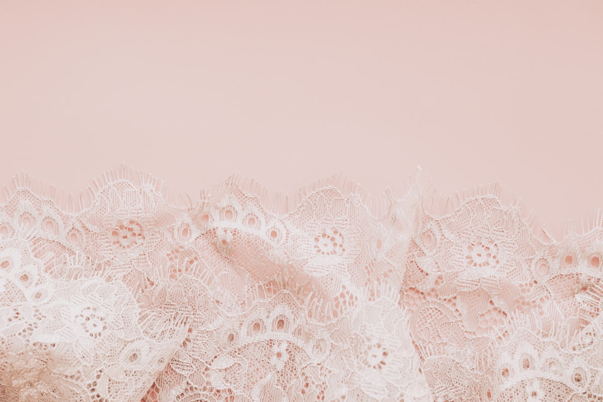 Delicate white lace fabric on a pale pink background related to White Lace Shower Curtain with Valance