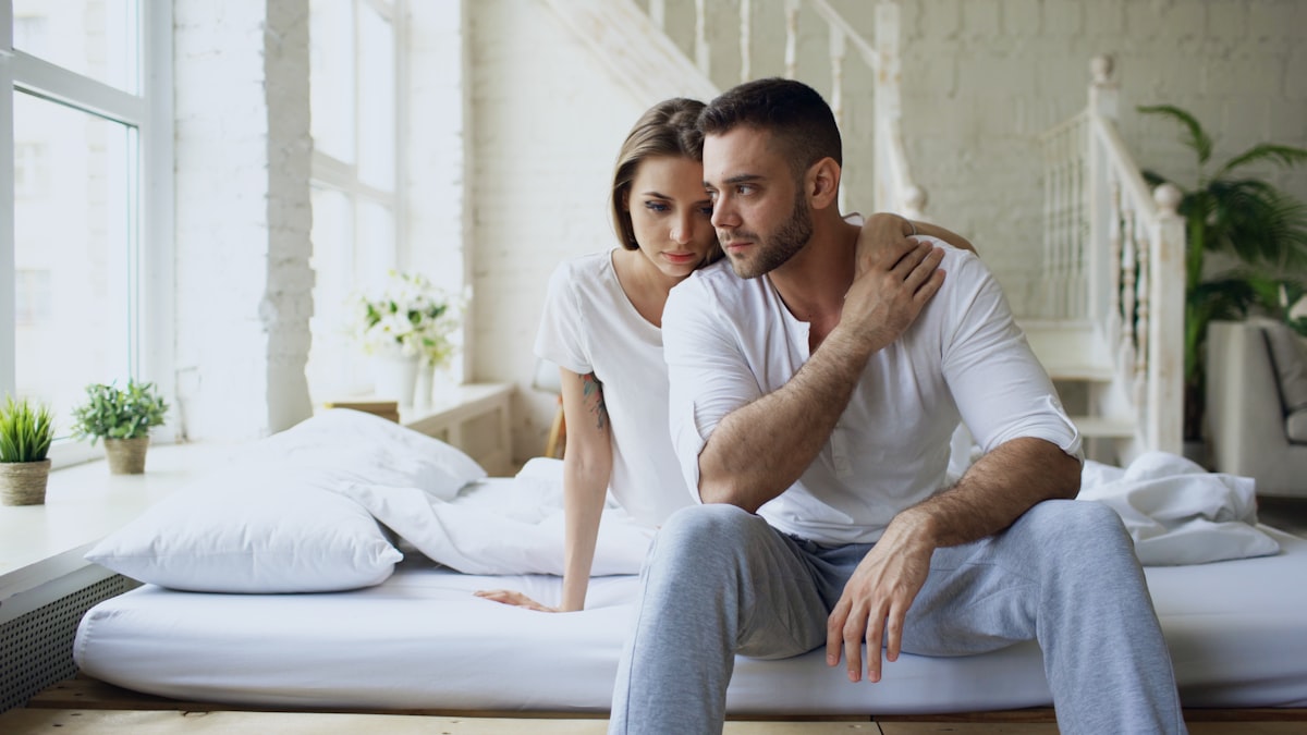 Depressed yong man sitting in bed having stressed while his girlfriend come and embrace him in bedroom at home related to Unlocking the Mystery: What Men Really Want in the Bedroom