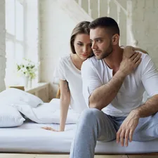 Depressed yong man sitting in bed having stressed while his girlfriend come and embrace him in bedroom at home related to Unlocking the Mystery: What Men Really Want in the Bedroom