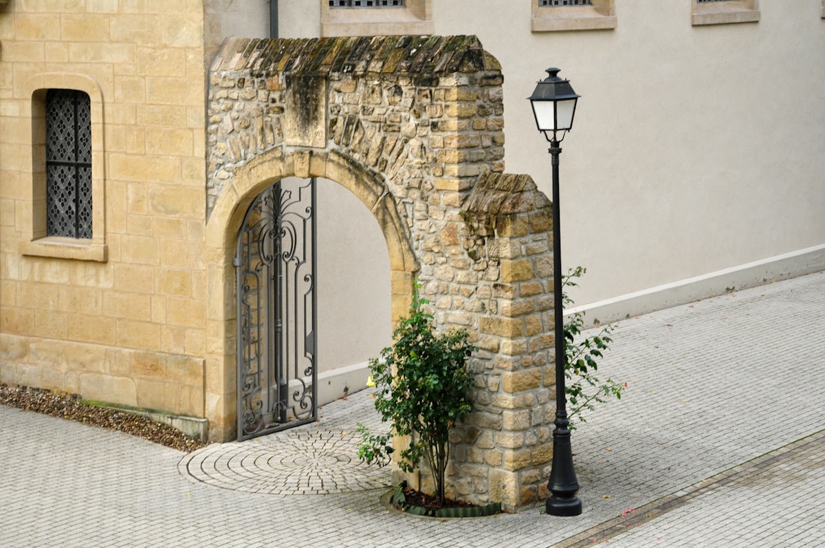 Elegant historic stone archway with an ornate wrought iron gate and a classic black street lamp on a cobblestone pavement. related to Revamping Your Home's Welcome: Outside Entryway Ideas