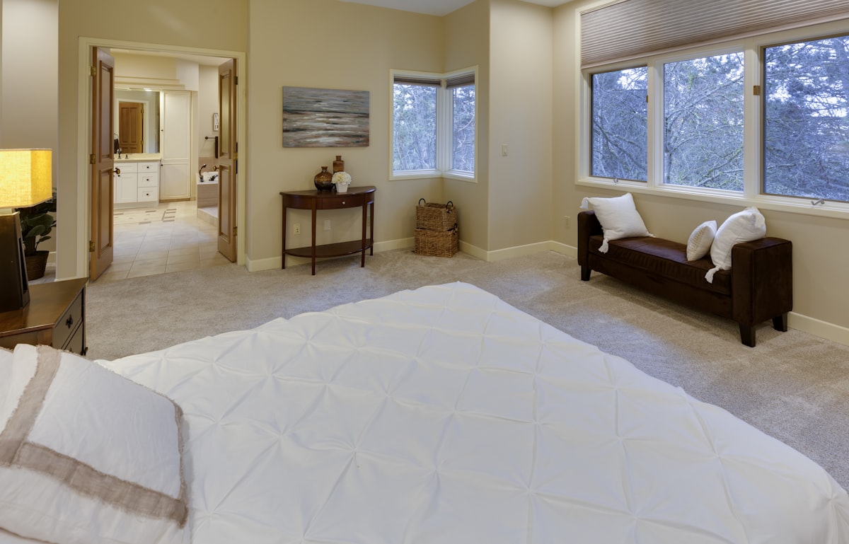 empty bed near open bathroom door related to Elevate Your Bedroom with an Ivory Coverlet for Your King-Size Bed