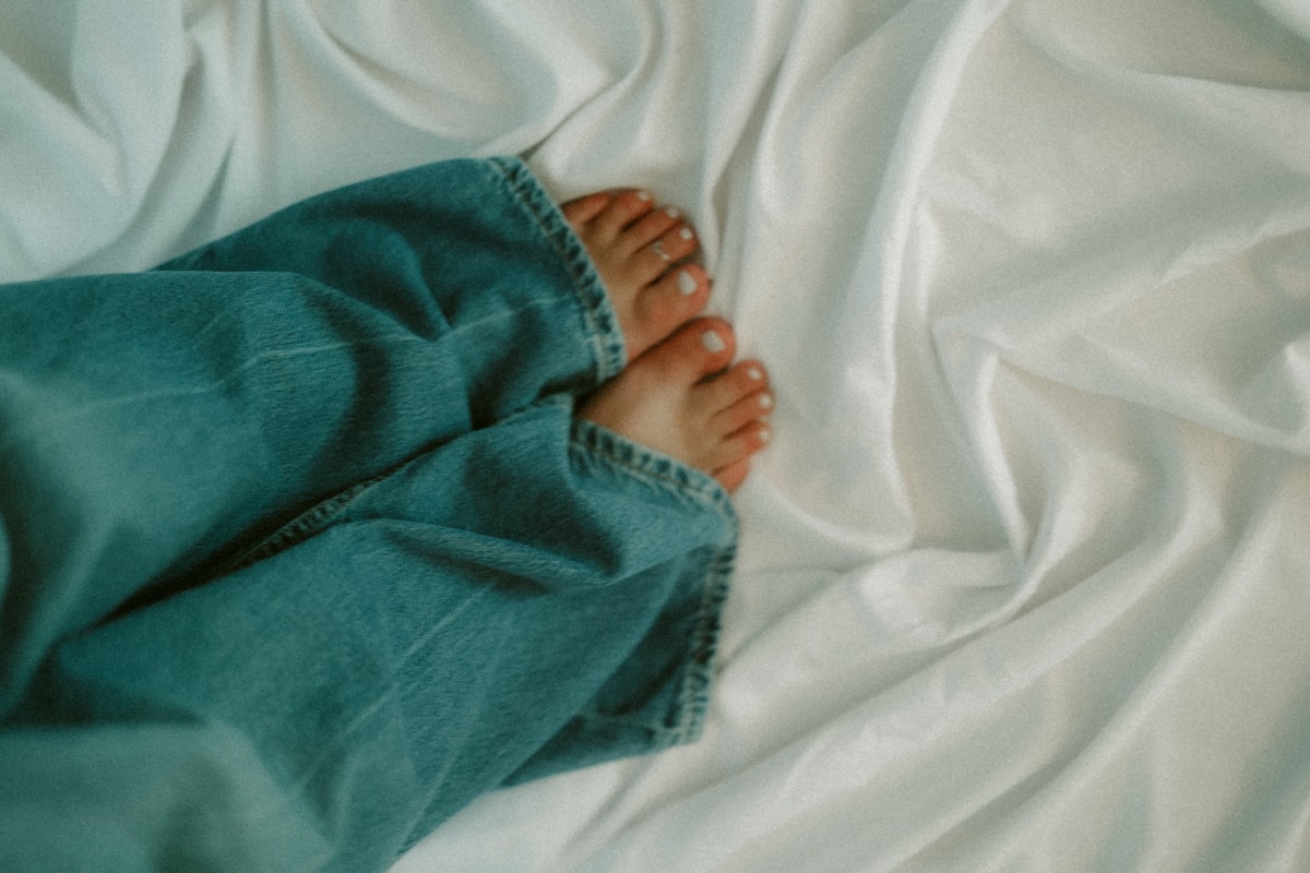 Feet and jeans relax on a soft, white bed. related to Everything You Need to Know About King Bed Size in Feet