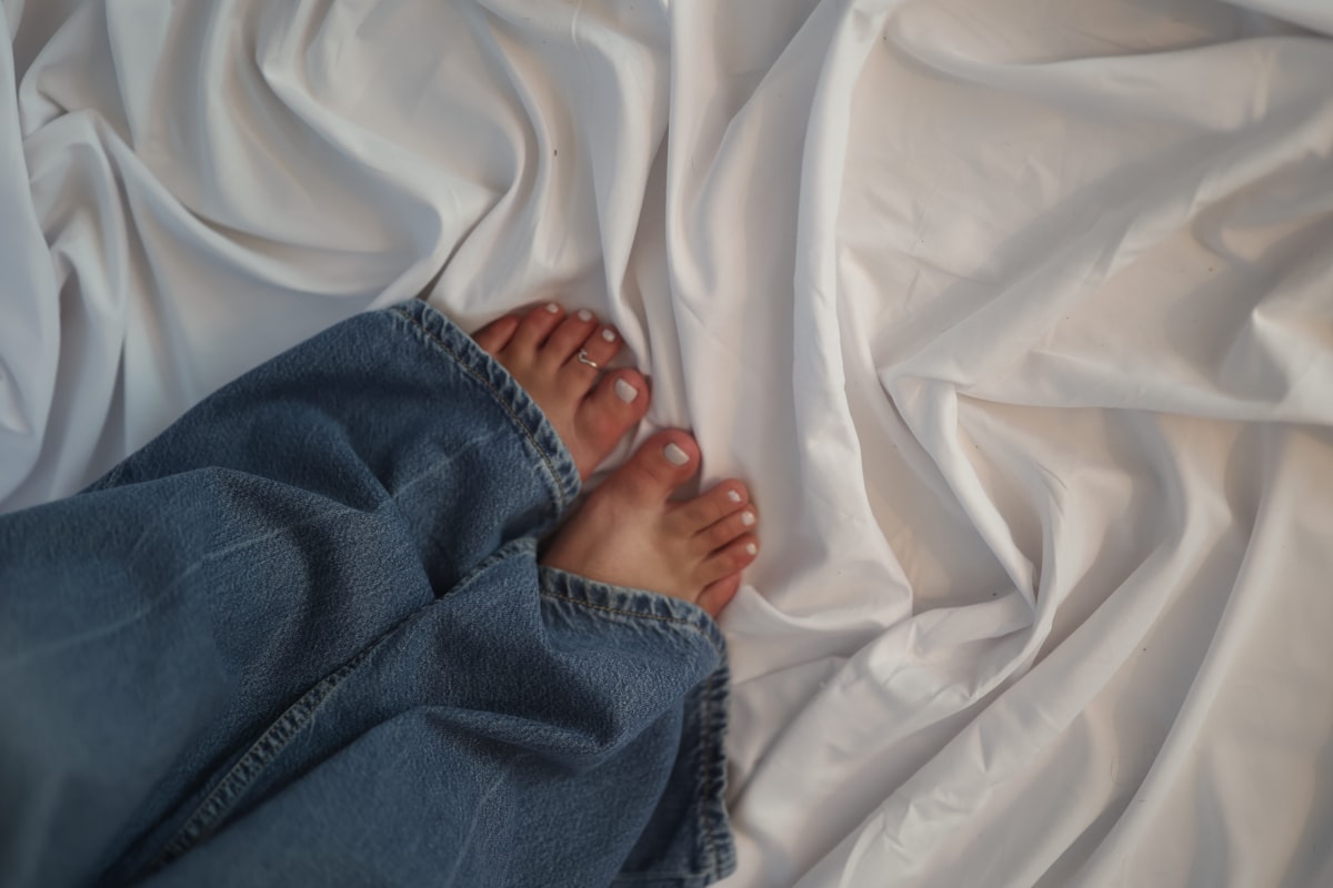 Feet in jeans rest on rumpled white fabric. related to Everything You Need to Know About King Bed Size in Feet