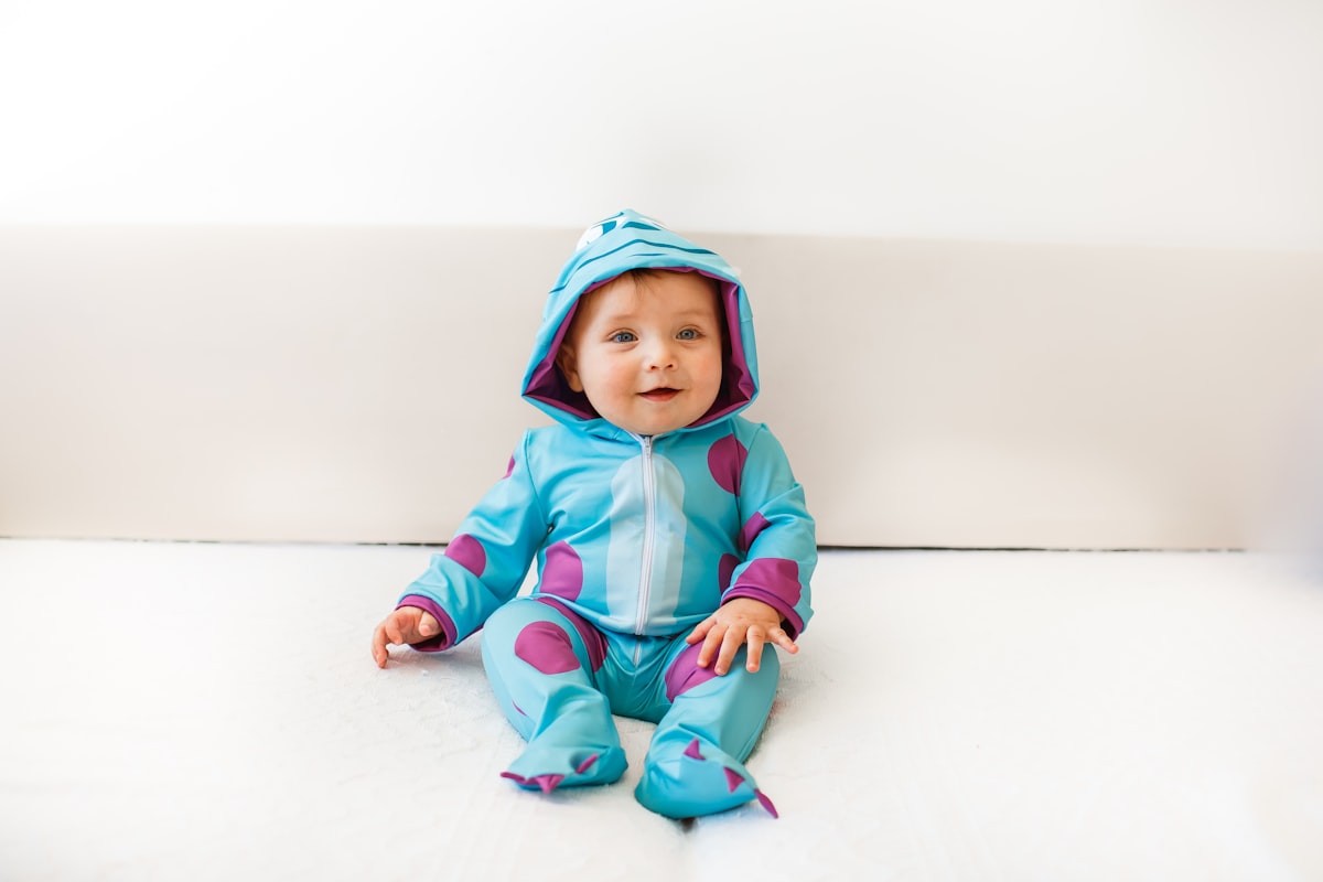 girl in pink hoodie and blue pants sitting on white floor related to Monster Baby Bedding: A Whimsical Way to Decorate Your Nursery