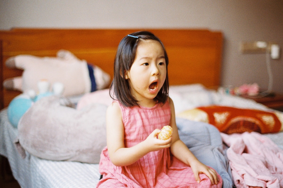 girl in pink sleeveless dress sitting on bed related to Sweet Dreams: The Ultimate Guide to Toddler Girl Bedding