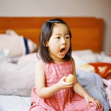girl in pink sleeveless dress sitting on bed related to Sweet Dreams: The Ultimate Guide to Toddler Girl Bedding