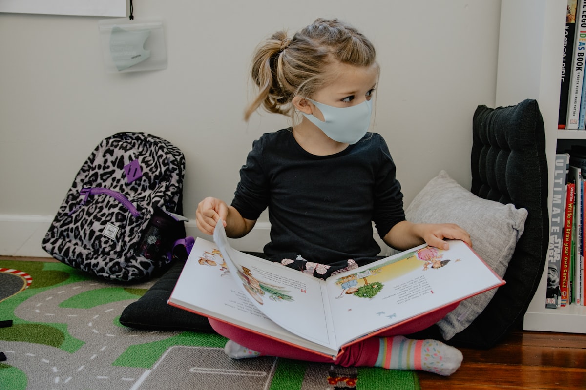 girl with mask on and backpack reading a book related to Secure Your Child's Safety with KidCo Bed Rail