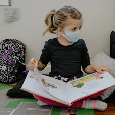 girl with mask on and backpack reading a book related to Secure Your Child's Safety with KidCo Bed Rail