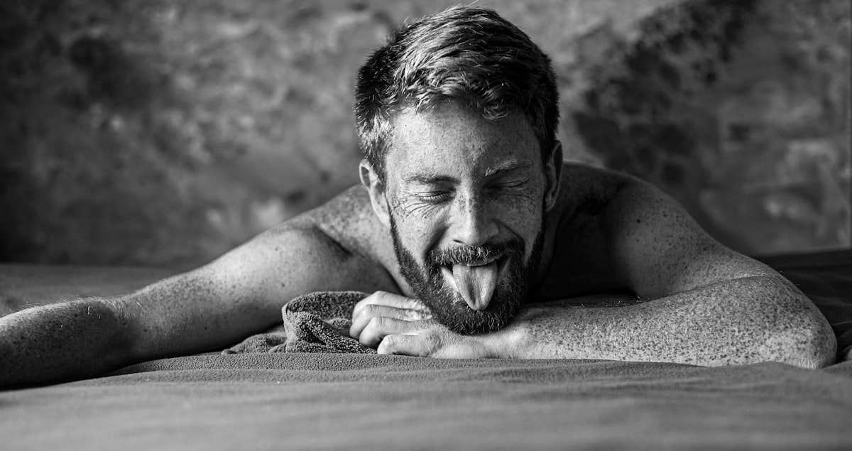 grayscale photo of man lying on wooden surface related to The Complexities of Male Intimacy