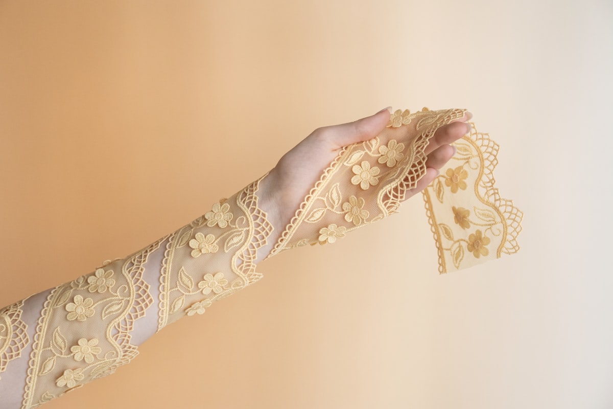Hand holding delicate yellow lace fabric with floral pattern. related to Vintage Lace Valances: A Touch of Elegance for Your Home