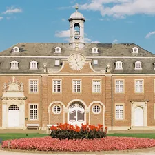 Historic palace facade symmetry analog photography architecture. Elegant European baroque-style building with red brick walls, central clock and flower garden, captured on Kodak Portra 800 film using a Contax camera related to Beautiful Flower Bed Designs for the Front of Your House