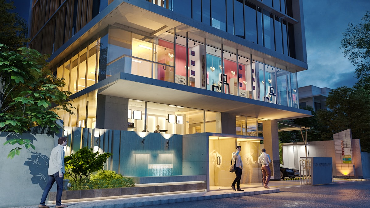 Image Description: This image captures a modern, multi-story building entrance at dusk. The ground floor features large glass windows, revealing a brightly lit interior with a contemporary, open-plan design. The upper floor is also visible through a large glass facade, showcasing colorful, abstract shapes and a vibrant lighting scheme that contrasts with the muted tones of the exterior. Outside, two men are walking towards the entrance, suggesting a residential or commercial setting. The building's exterior is sleek, with a combination of glass, concrete, and what appears to be wooden or metal related to Transform Your Curb Appeal: Outdoor Entryway Ideas to Wow