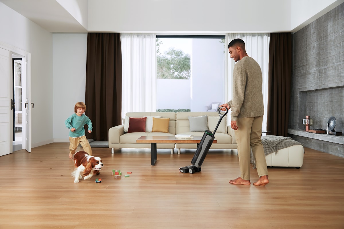 In a sunlit living room, a man uses a Dreame wet dry vacuum while his child and dog play nearby, creating a family-friendly cleaning moment. related to Elevate Your Home with Black and White Curtain Valance