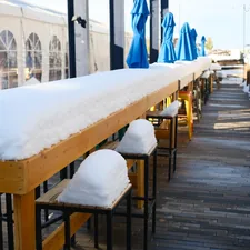Long outdoor bar covered in snow with blue umbrellas. related to Warm Up Your Outdoor Space with a Chiminea Fireplace