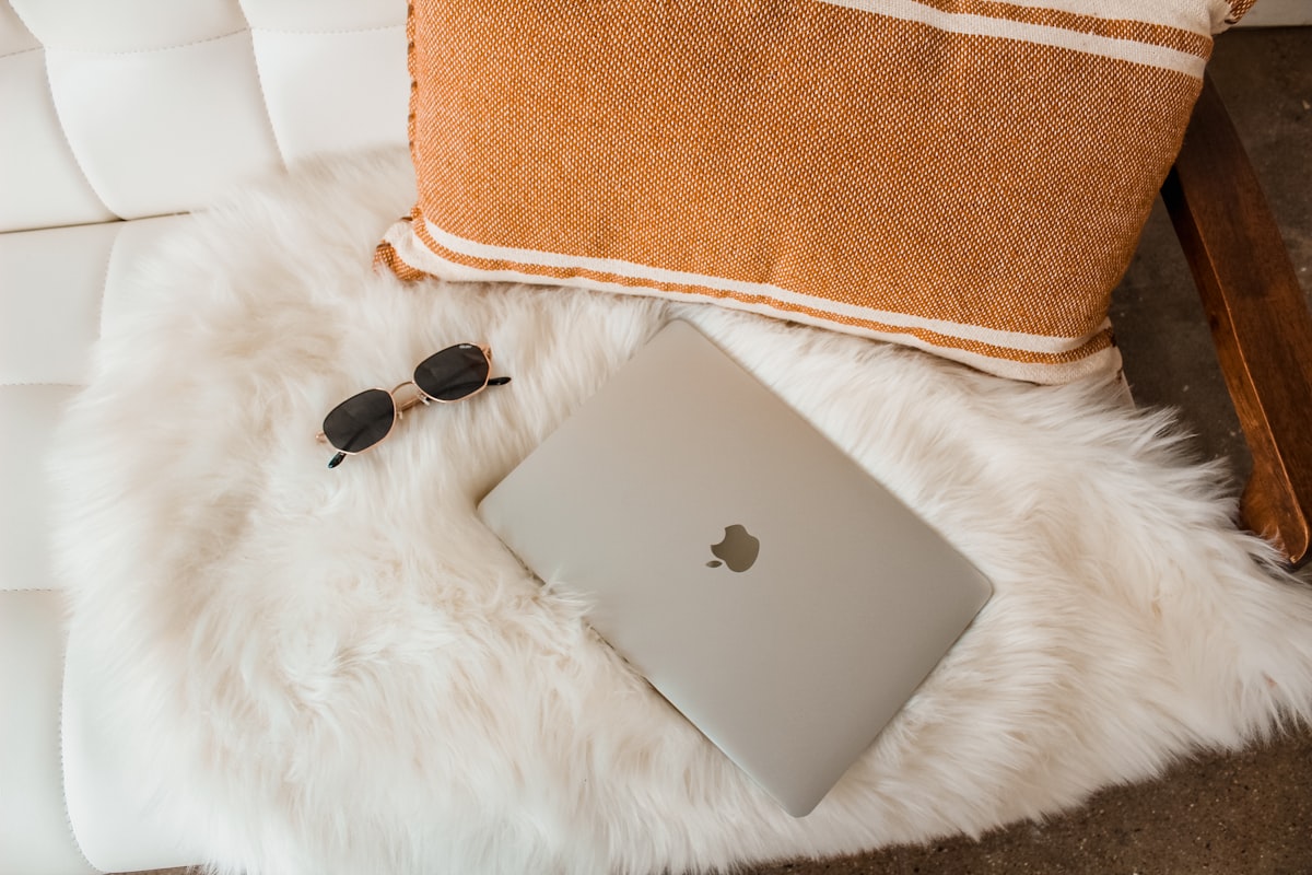 Macbook laptop on couch with fur blanket related to Sleeping in Style: The Comfort of Sheepskin Bed Pads