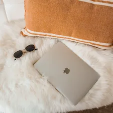 Macbook laptop on couch with fur blanket related to Sleeping in Style: The Comfort of Sheepskin Bed Pads