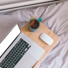 macbook pro beside white ceramic mug on white textile related to Elevate Your Sleeping Experience with Computer Tables for Bed