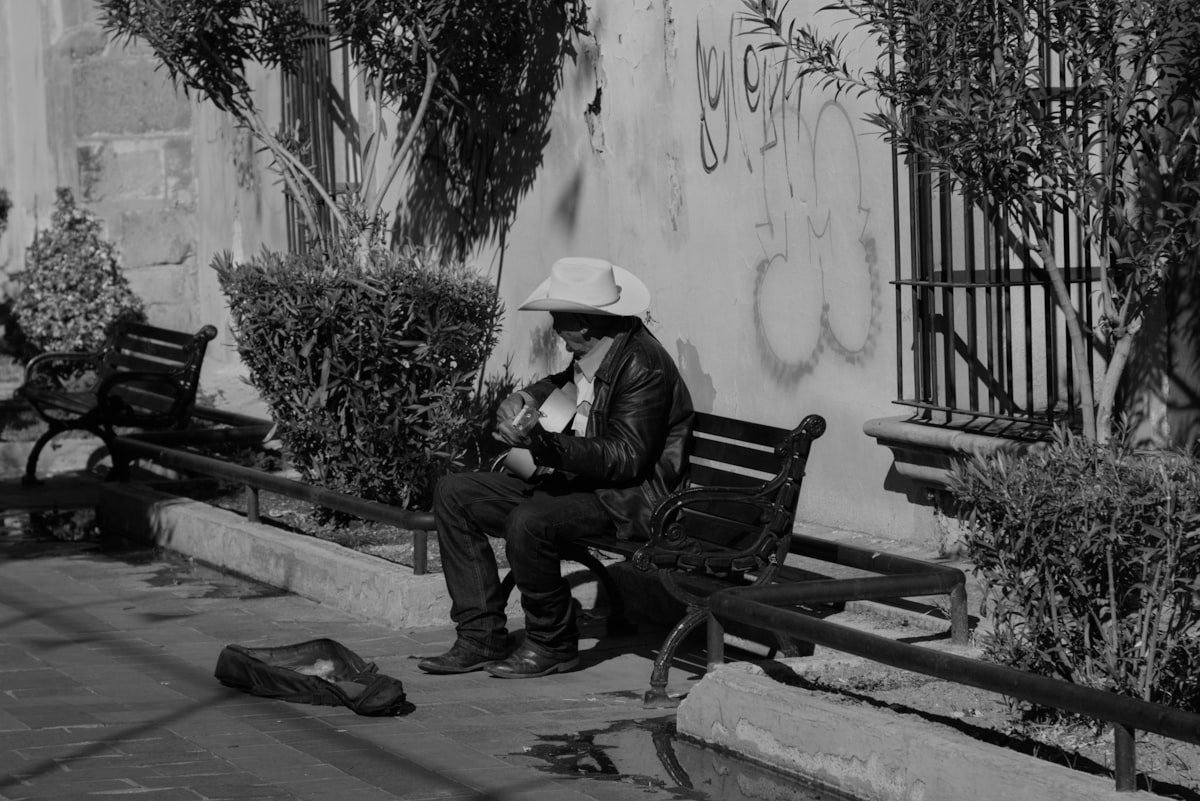 Man in cowboy hat sits on park bench with guitar. related to Discover the Urban Cowboy Bed and Breakfast Experience