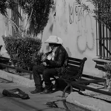 Man in cowboy hat sits on park bench with guitar. related to Discover the Urban Cowboy Bed and Breakfast Experience