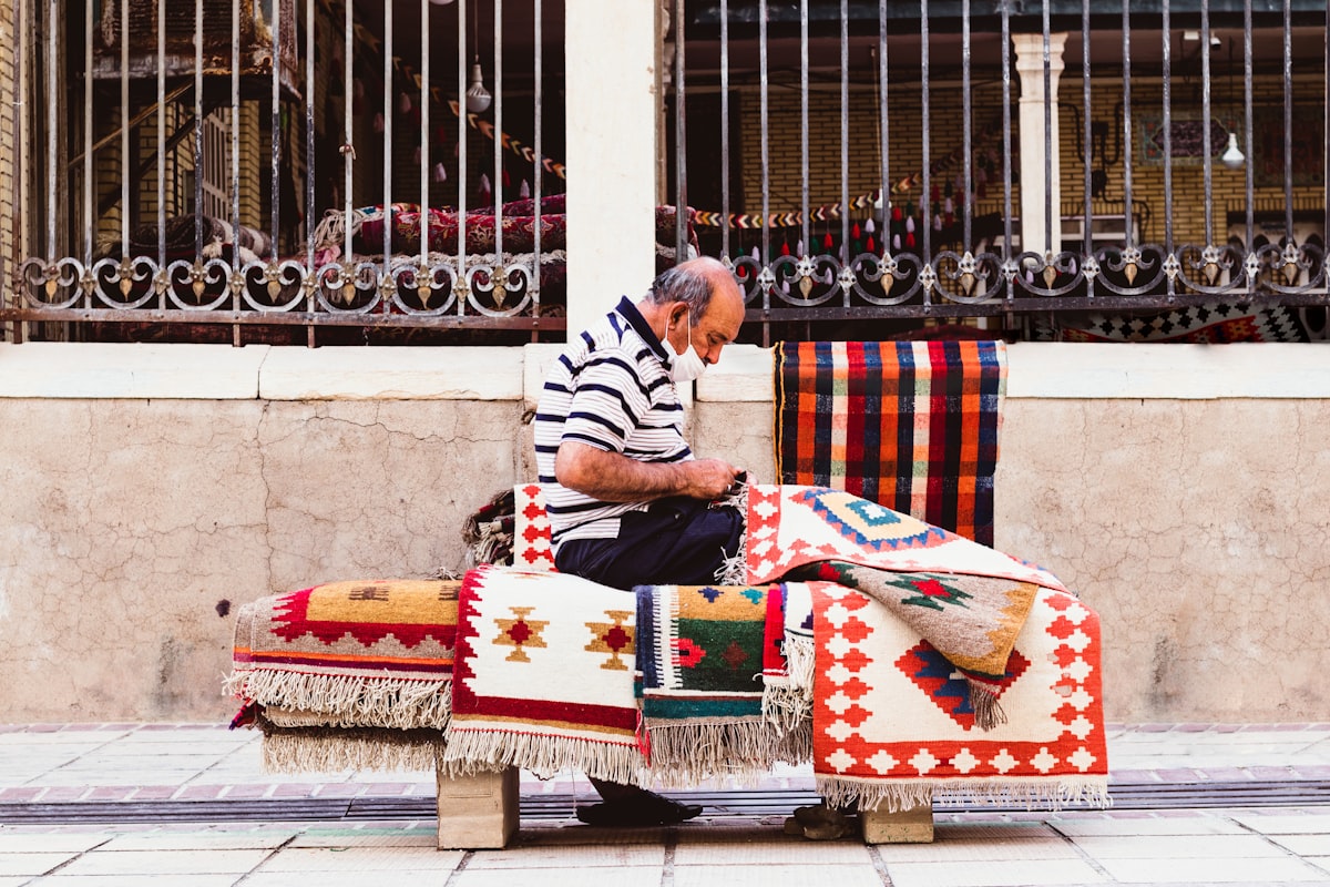 man in white and black stripe long sleeve shirt sitting on white red and blue textile related to The Ultimate Guide to Coverlet Quilts: History, Types, and Uses
