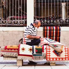 man in white and black stripe long sleeve shirt sitting on white red and blue textile related to The Ultimate Guide to Coverlet Quilts: History, Types, and Uses