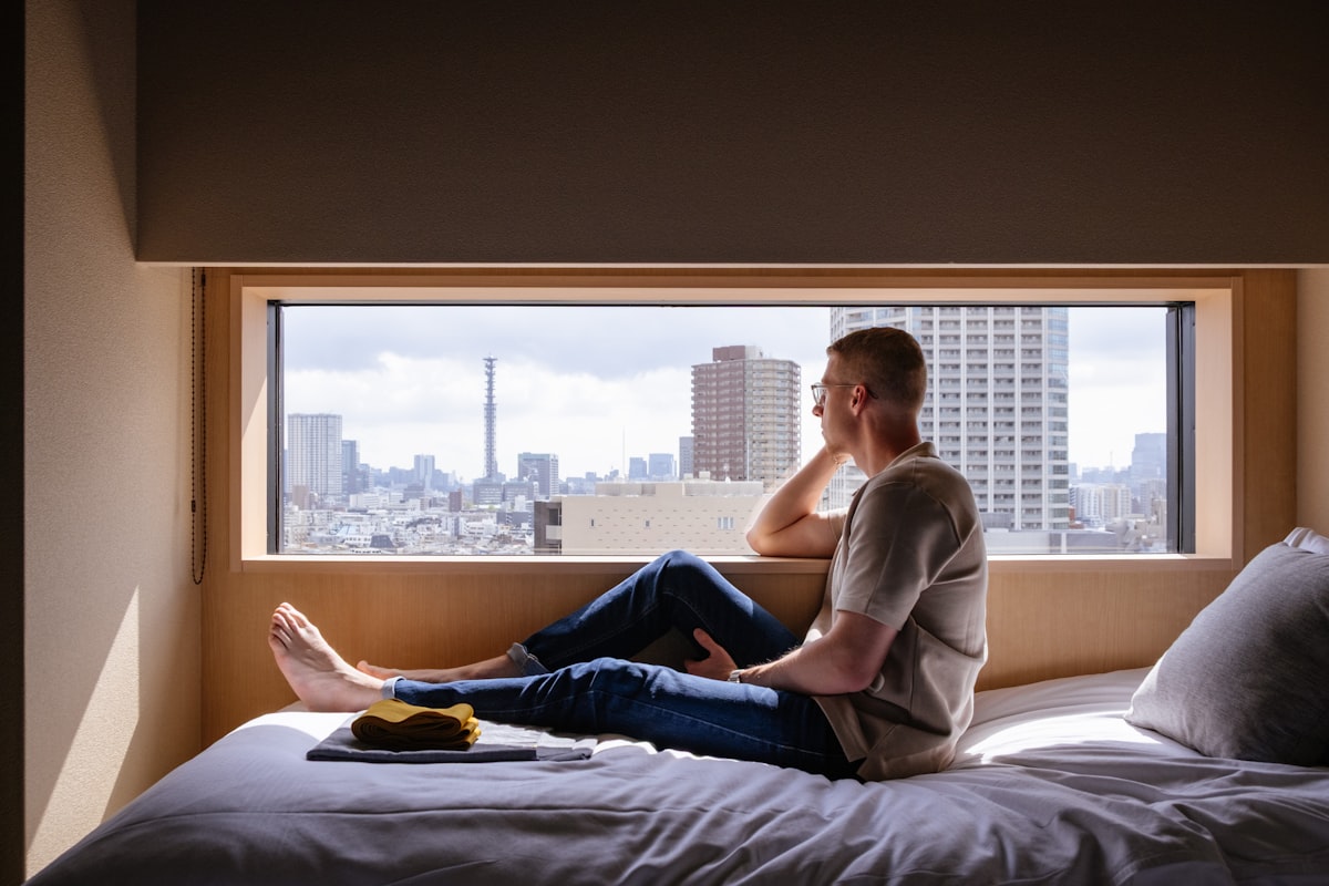 Man relaxes on a bed, gazing at a city view. related to Maximizing Space and Comfort: The Full Bed with Pull Out Bed