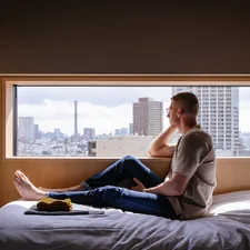 Man relaxes on a bed, gazing at a city view. related to Maximizing Space and Comfort: The Full Bed with Pull Out Bed